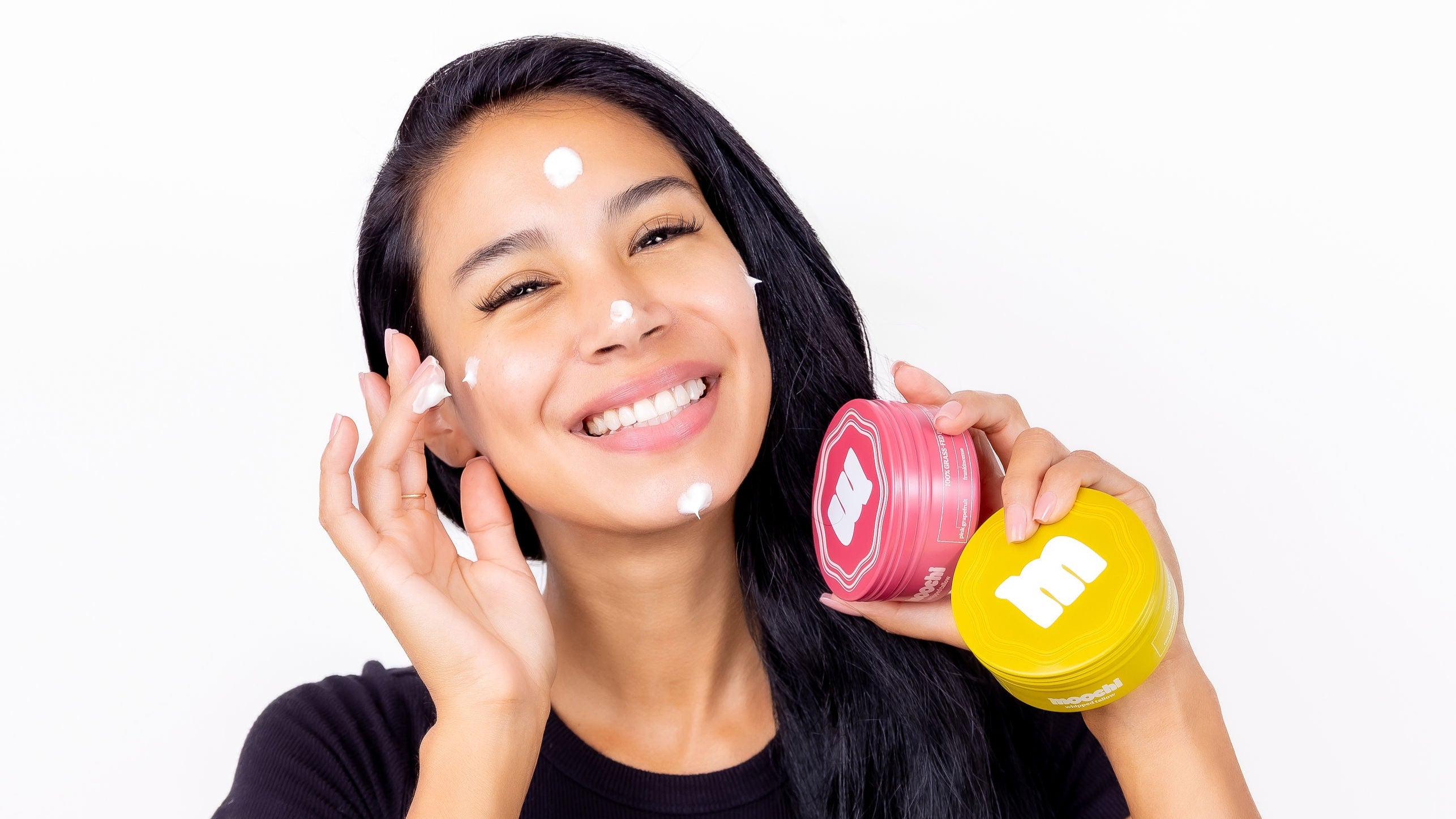 Woman applying beef tallow cream to her face with skincare products on a white background